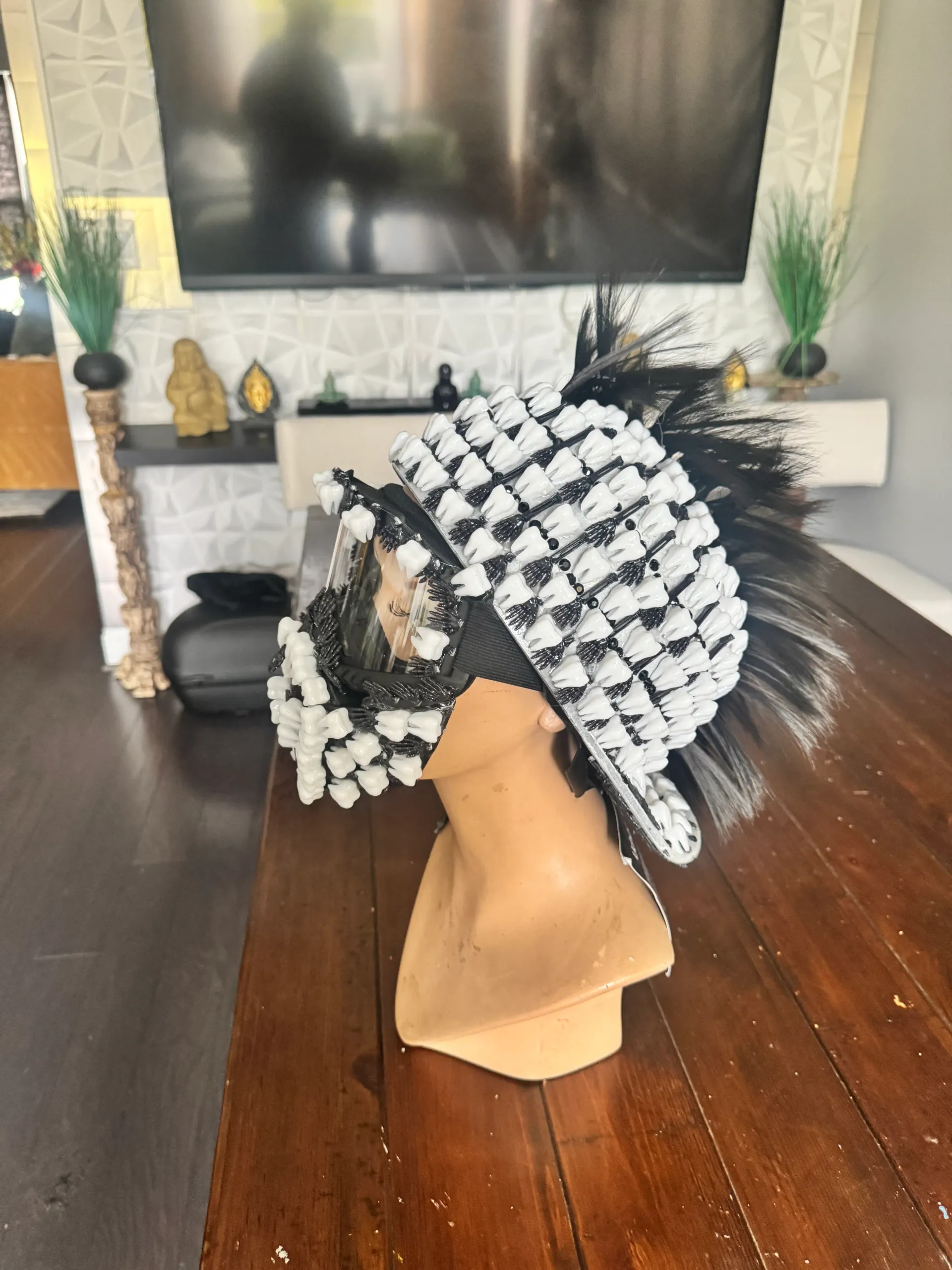 Casual indoor front view of the black teeth helmet with a clear visor and feather mohawk on a mannequin bust